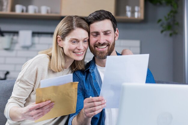 Happy married couple man and woman received a positive letter sitting at home on the couch smiling and rejoicing