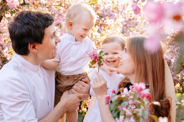 Happy married couple with children joyfully look at pink flowers of apple tree in the park