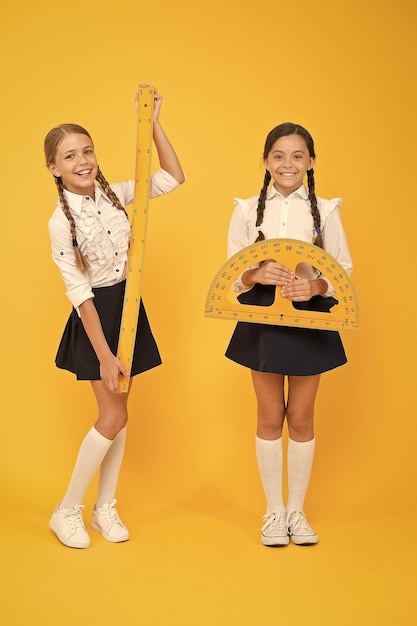 Happy math stem disciplines back to school Maths and geometry Kids in uniform at yellow wall friendship and sisterhood happy small girls study mathematics students use protractor ruler