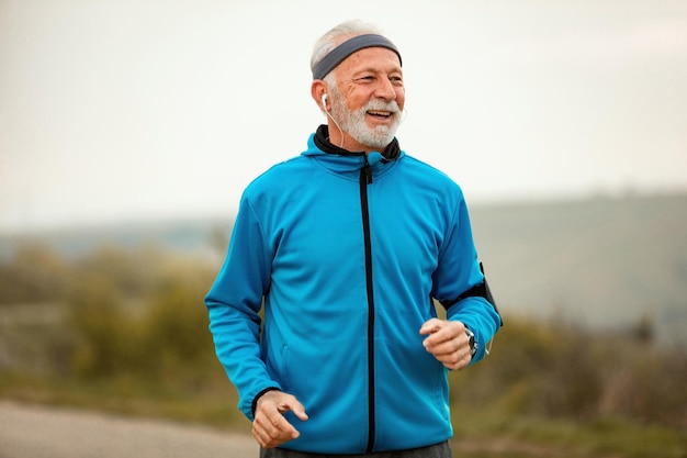 Happy mature athletic man jogging in nature while listening music on earphones