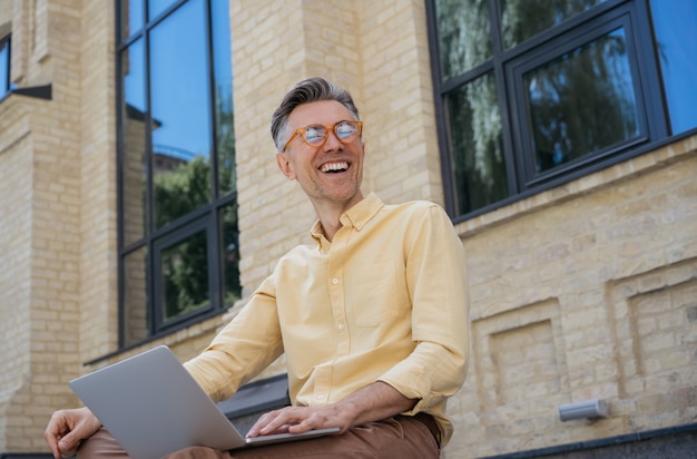 Happy mature businessman using laptop, typing on keyboard, laughing