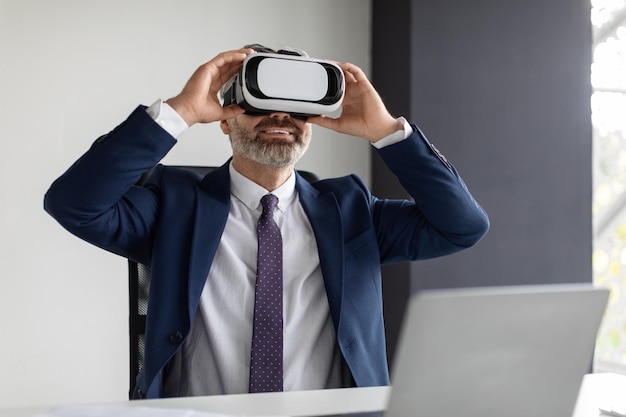 Happy Mature Businessman In VR Headset Having Fun At Workplace In Office