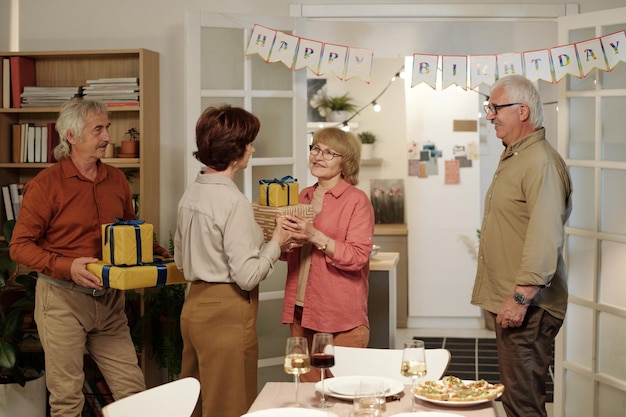 Happy mature couple giving packed and wrapped giftboxes to aged woman