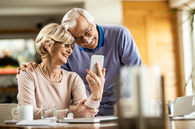 Happy mature couple having fun while using smart phone and taking selfie at home