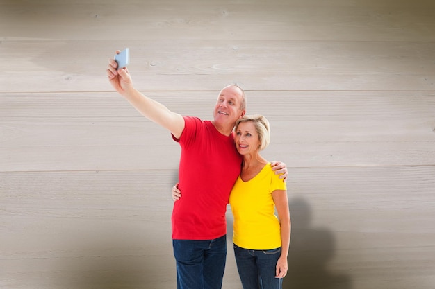 Happy mature couple taking a selfie together against bleached wooden planks background