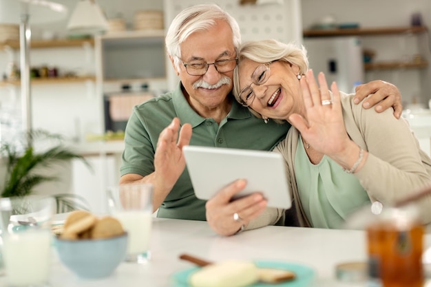 Happy mature couple waving while making video call over digital tablet