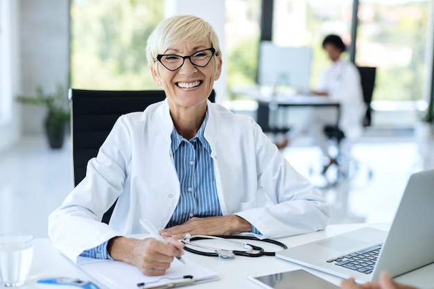 Happy mature doctor working at her office ad looking at camera