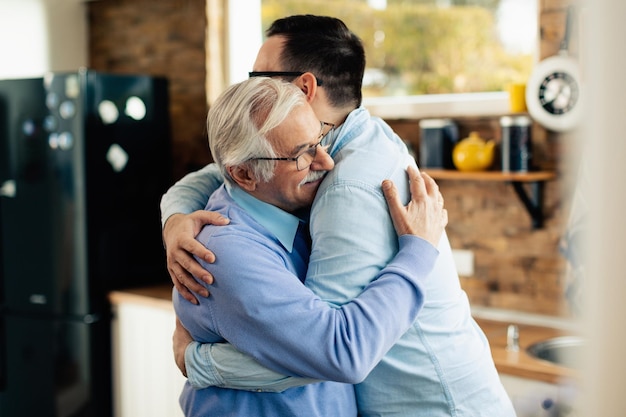 Happy mature father greeting his adult son and embracing him in the kitchen