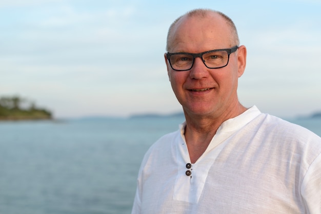 Happy mature handsome tourist man smiling against view of the beach outdoors