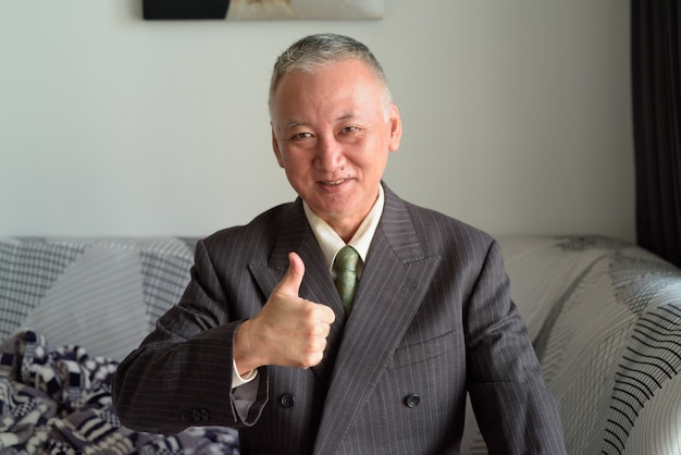 Happy mature Japanese businessman smiling and giving thumbs up at home