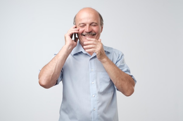 Happy mature man bald and with mustache talking on mobile isolated on white background