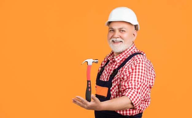 Happy mature man carpenter in helmet on yellow background