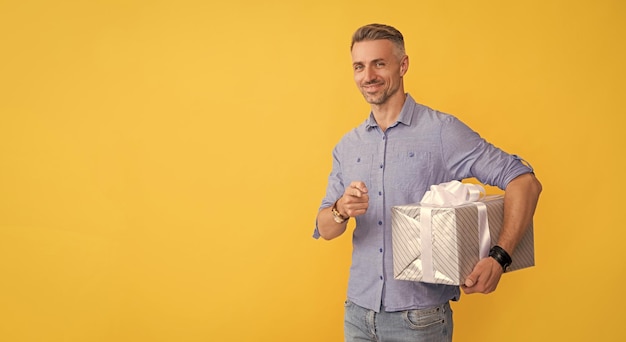 Happy mature man hold box pointing finger on yellow background copy space shopping