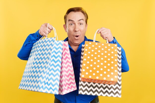 Happy mature man looking at the camera showing shopping bags