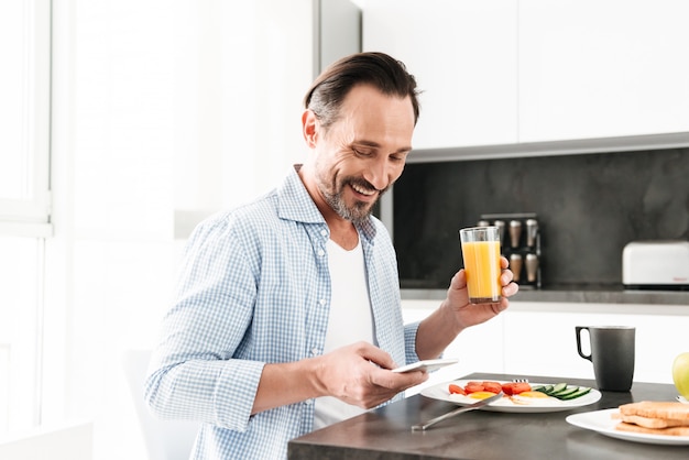 Happy mature man using mobile phone while having breakfast