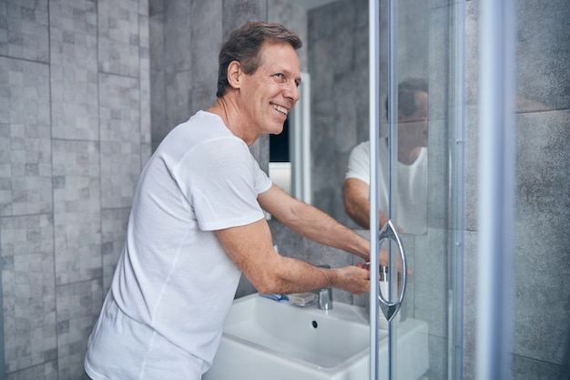 Happy mature man with his hand on the pump bottle standing in a bathroom