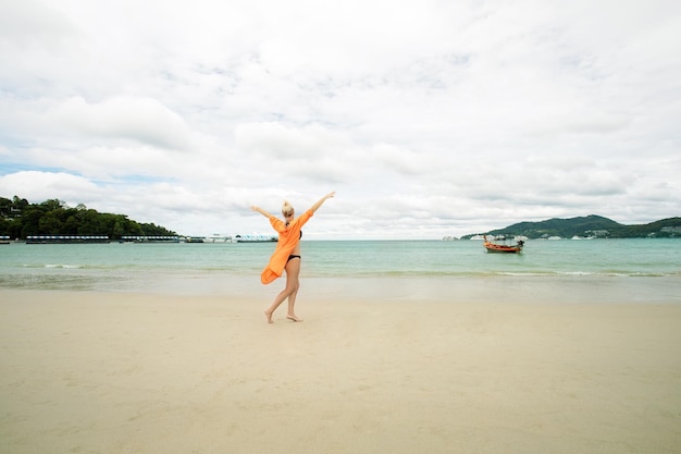 Happy mature woman in dress dancing on the beach Woman enjoying beautiful summer vacation