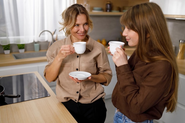 Happy mature woman enjoying in coffee with her adult daughter at the kitchen