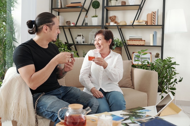 Happy mature woman and her adult son drinking tea and discussing latest news