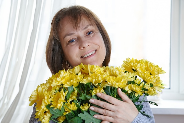 Happy mature woman holding an armful of yellow flowers