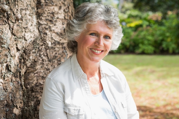 Happy mature woman sitting on tree trunk