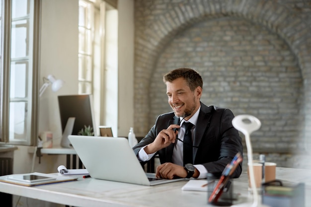 Happy mid adult entrepreneur surfing the net on a computer in the office