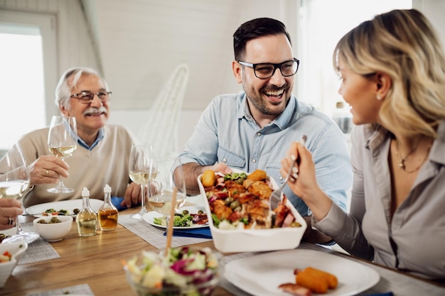 Happy mid adult man talking to his wife while passing her food during family lunch at home