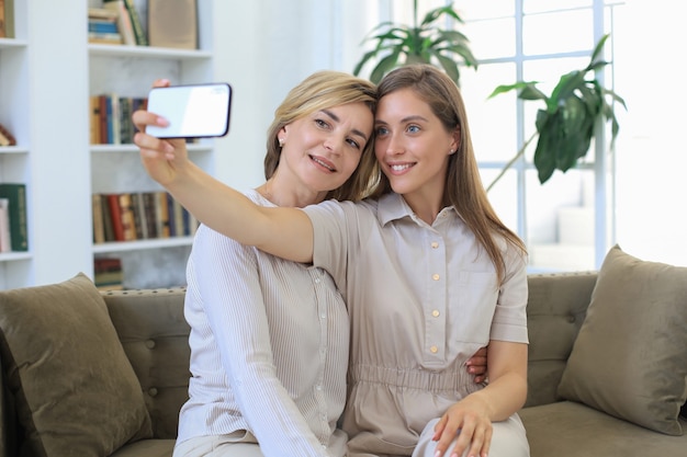 Happy middle aged mother and daughter taking selfie at home.