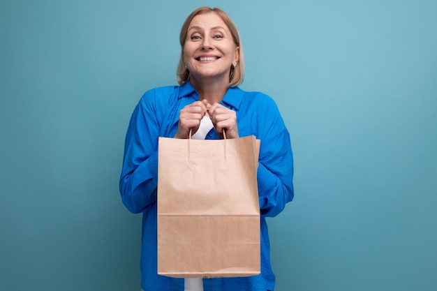 Happy middle aged woman holding craft eco friendly bag on blue copy space background