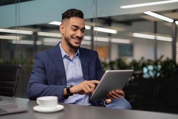 Happy middle eastern businessman working at office using digital tablet