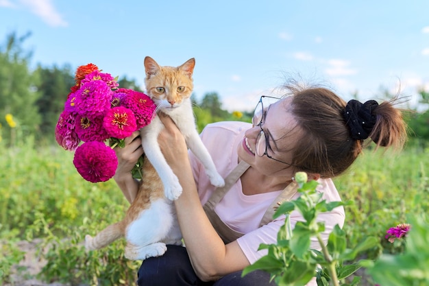 Happy middleaged woman with pet red cat in her arms and bouquet of flowers