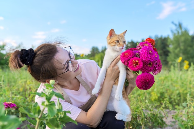 Happy middleaged woman with pet red cat in her arms and bouquet of flowers