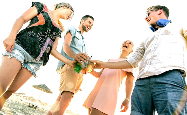 Happy millenial friends group having fun at beach party drinking fancy cocktails at sunset