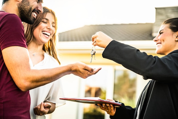 Happy millennial couple receiving keys from realtor purchasing real estate