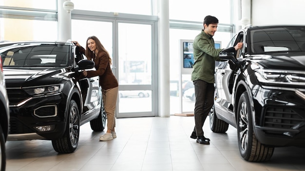 Happy millennial couple selecting new car buying or renting automobile at auto dealership banner