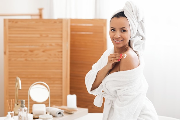 Happy mixed lady moisturizing shoulders caring for body in bathroom