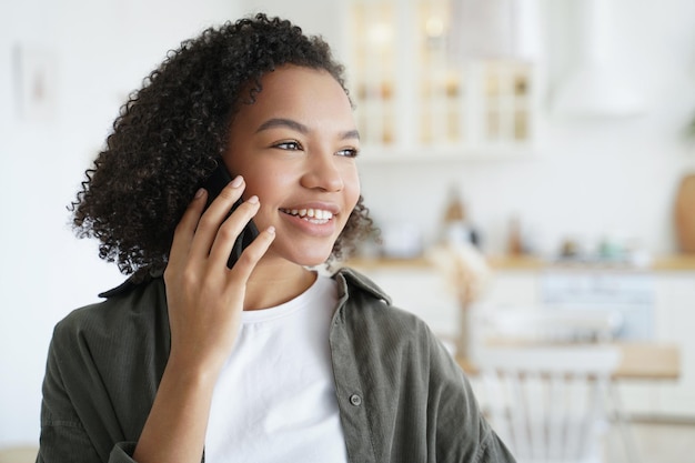 Happy mixed race girl answers call talking on phone enjoy pleasant mobile conversation at home