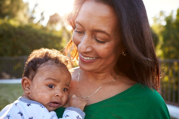 Happy mixed race middle aged grandmother holding her three month old grandson in the garden close up head and shoulders