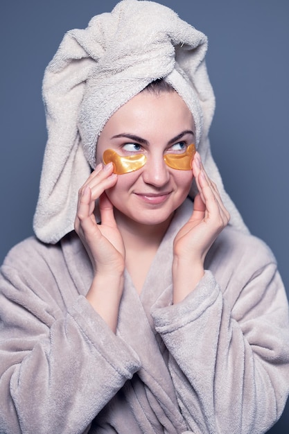 Happy modern woman with eye patches. Girl in a towel on her head, beauty, skin care.