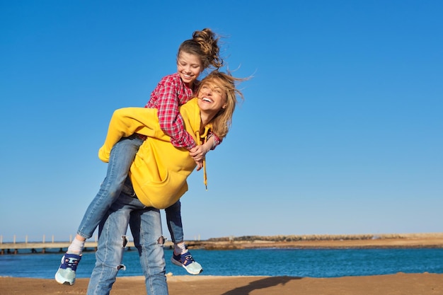 Happy mom and daughter child on seashore relaxing on sandy beach autumn winter spring season