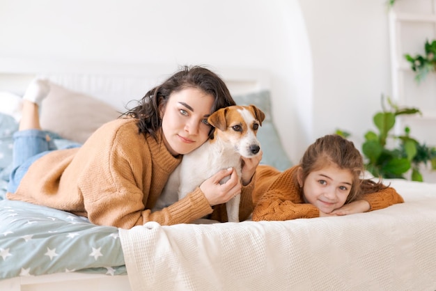 Happy mom and daughter play with their adorable wired Jack Russell Terrier