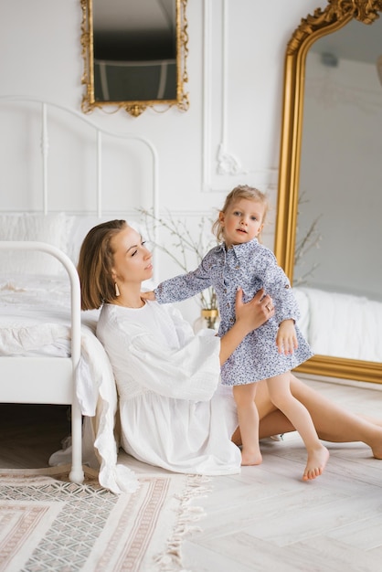 Happy mom is sitting by the bed and wants to hug her daughter