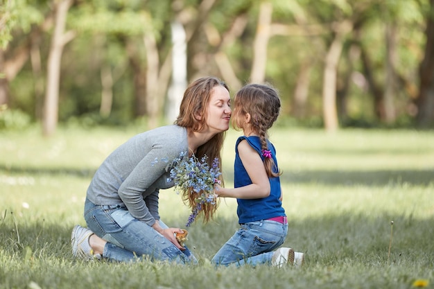 Happy mom and little daughter sitting on the lawn in the park