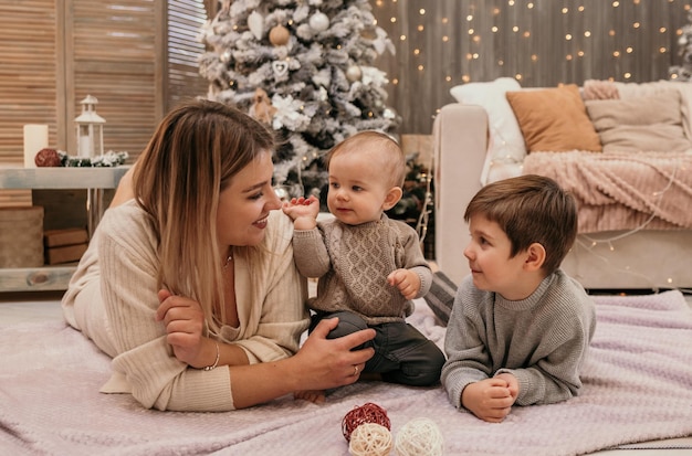 Happy mom and sons are lying on a blanket in the room near the Christmas tree