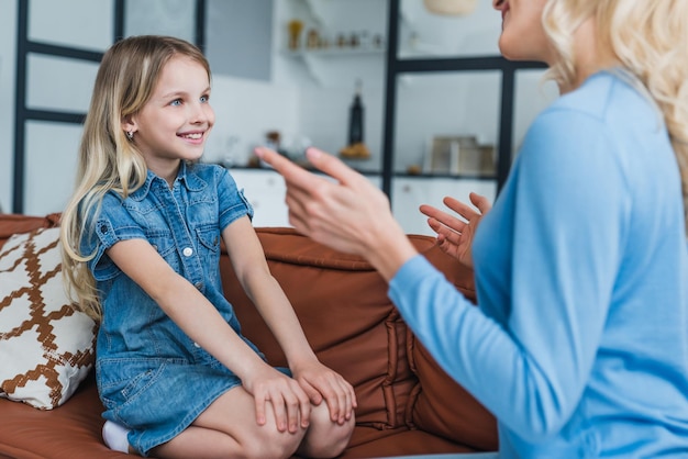 Happy mother and cute child girl talking sitting on sofa at home