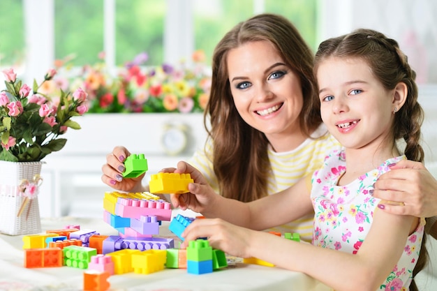 Happy mother and daughter collecting colorful plastic blocks