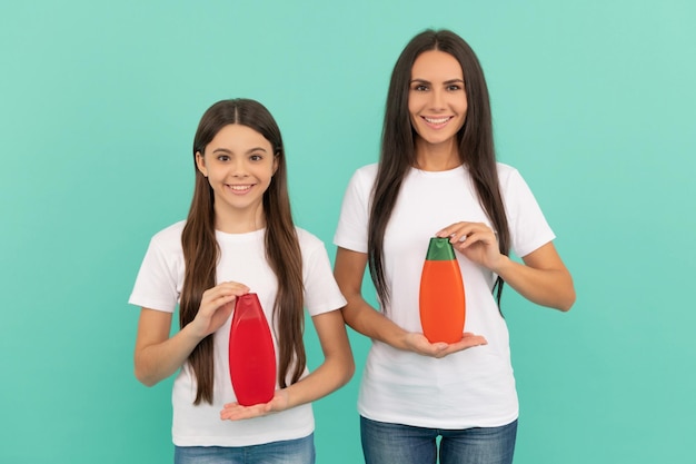 Happy mother and daughter hold shampoo bottle on blue background copy space