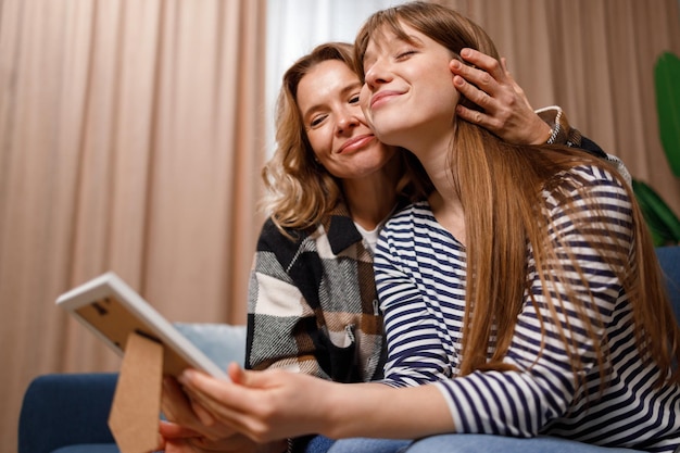 Happy mother and daughter hugging while sitting on sofa and looking at framed photo