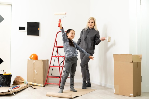 Happy mother and daughter makes repairs at home. Smiling woman and girl painting on wall at room.