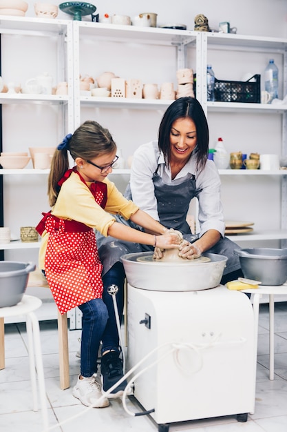 Happy mother and daughter making clay pottery on a spin wheel.